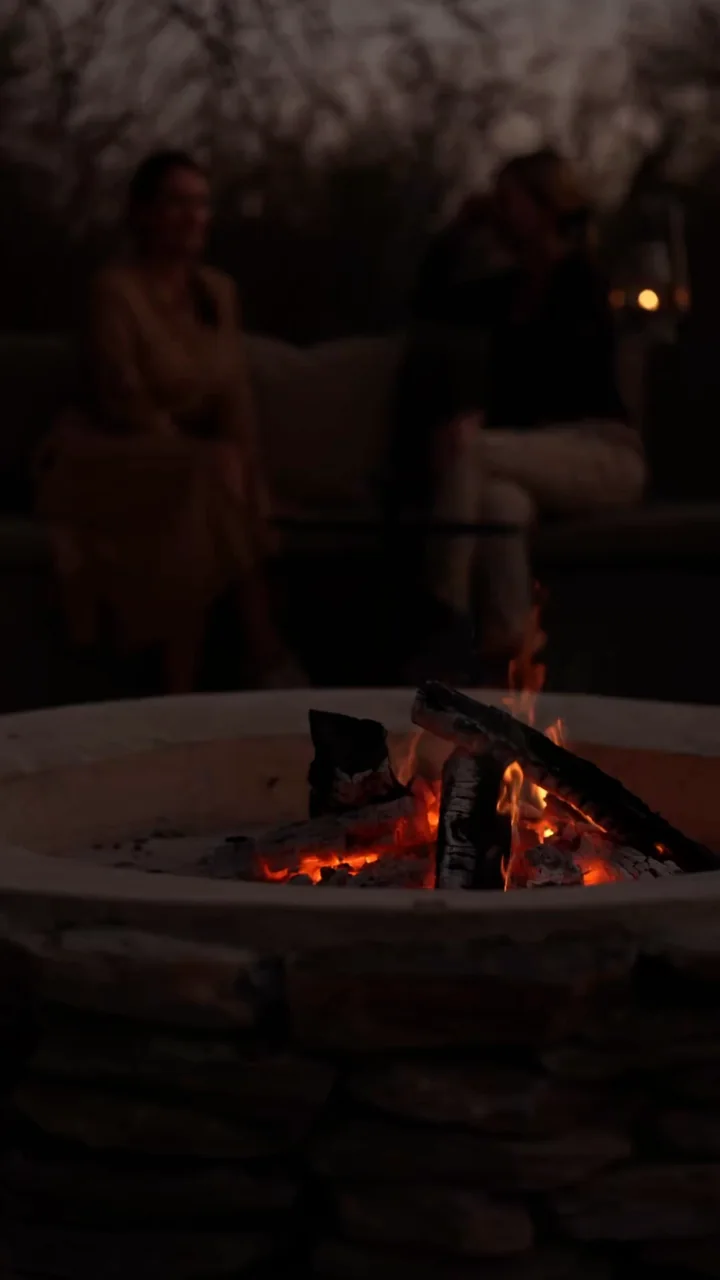 Flames in Ujima’s fire pit, with guests relaxing in the background at dusk.